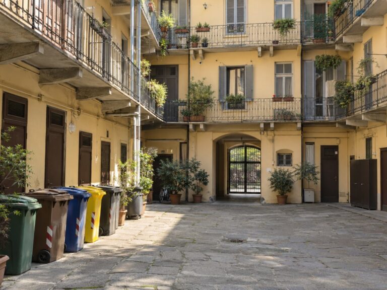 Cortile interno di un condominio torinese con ballatoi, porte delle cantine e bidoni della raccolta